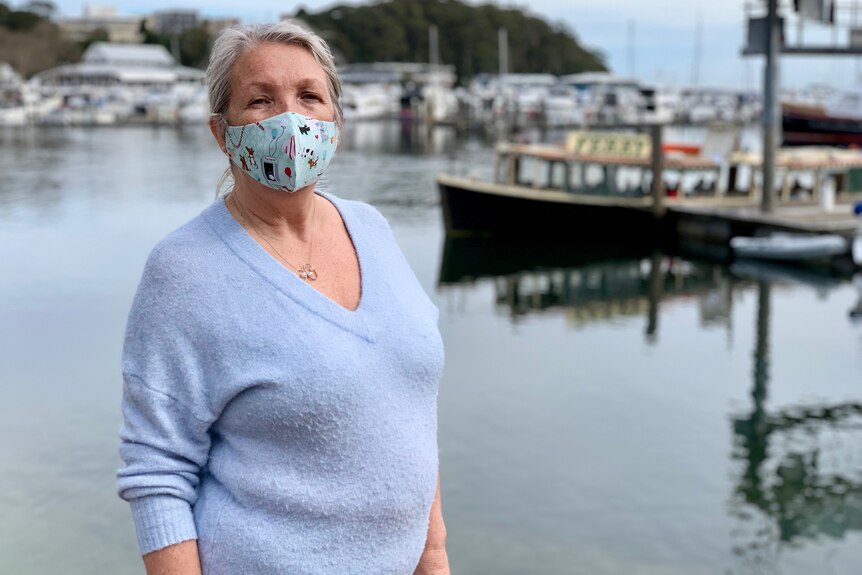 A woman with a mask on with a boat in harbour in the background