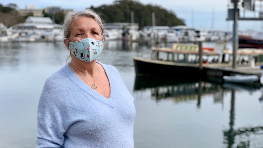 A woman with a mask on with a boat in harbour in the background