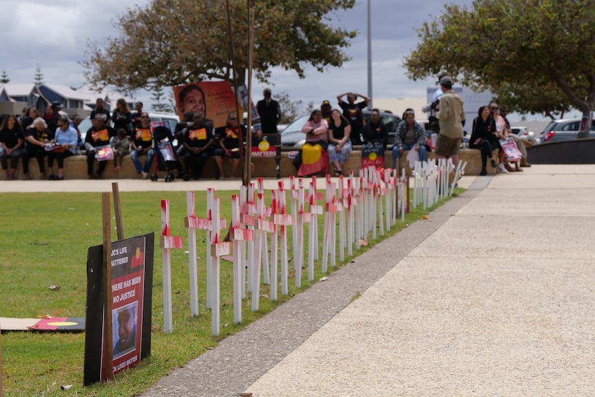 White crosses painted red lined up with protesters in the background