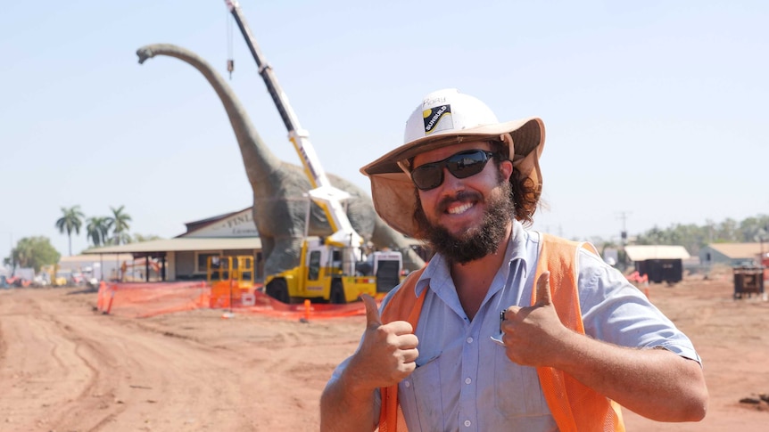 Man in high-vis gear smiling with dinosaur in background.