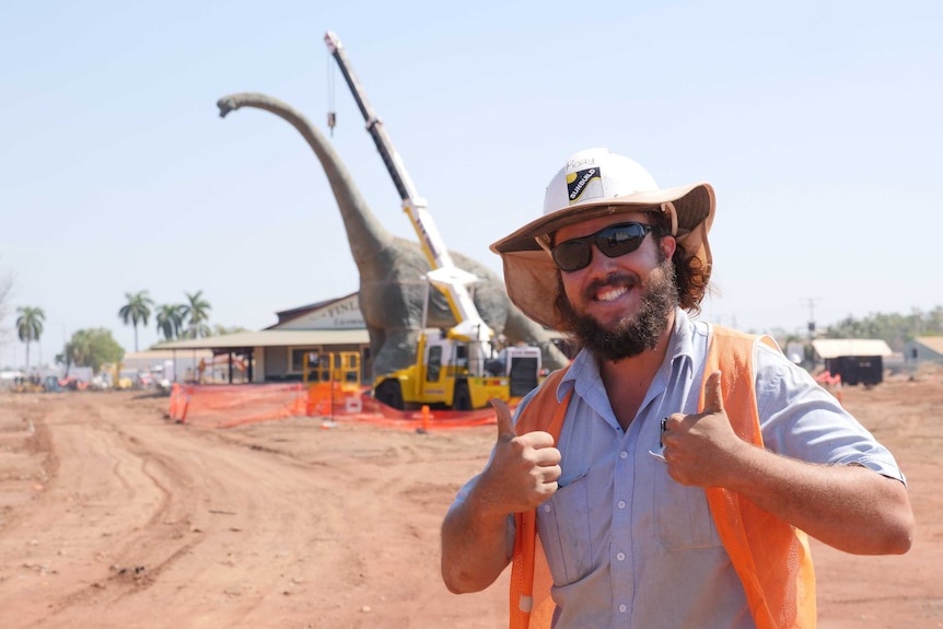 Man in high-vis gear smiling with dinosaur in background.