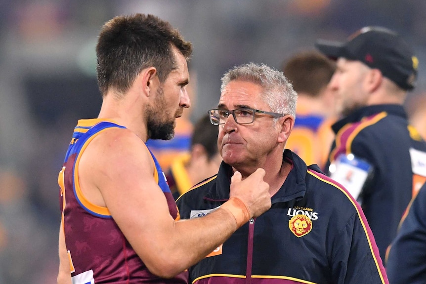 A sweaty Luke Hodge talks to Chris Fagan, wearing a Brisbane Lions jumper, on the sidelines.