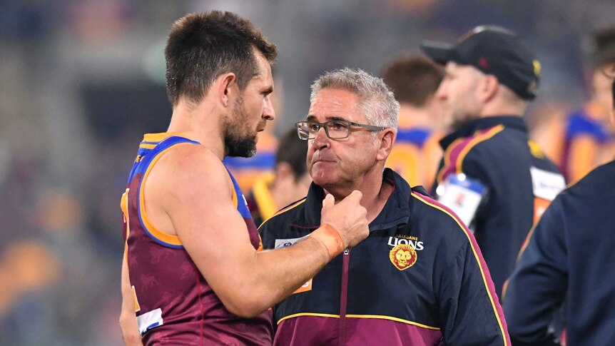 A sweaty Luke Hodge talks to Chris Fagan, wearing a Brisbane Lions jumper, on the sidelines.