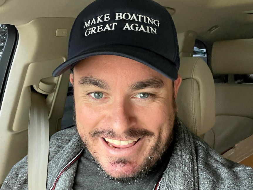 A man smiles. He wears a cap with the words "Make boating great again".