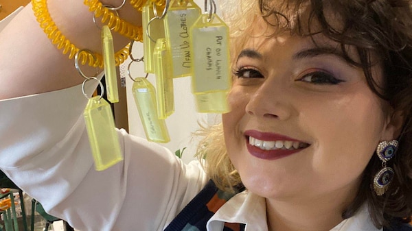 A woman smiling and holding up her wrist showing several yellow curly bracelets with key tags on them.