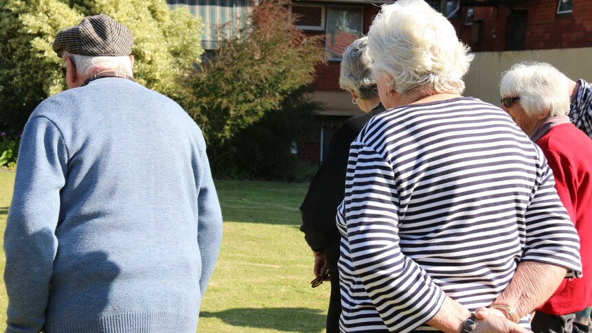 A group of older people outside playing lawn bowls.