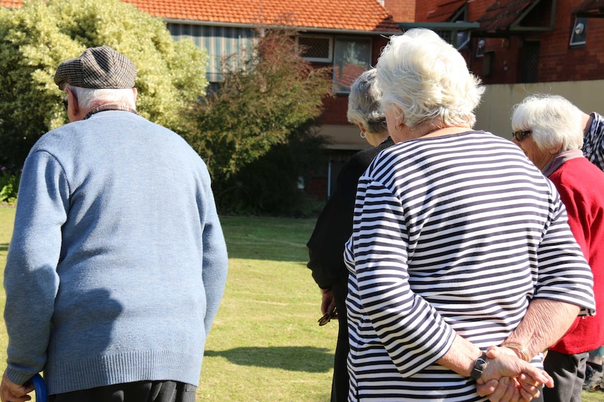 A group of old people walk across the lawn.