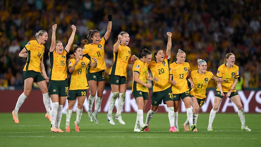 A group of women wearing yellow and green uniforms standing in a line jump in the air celebrating