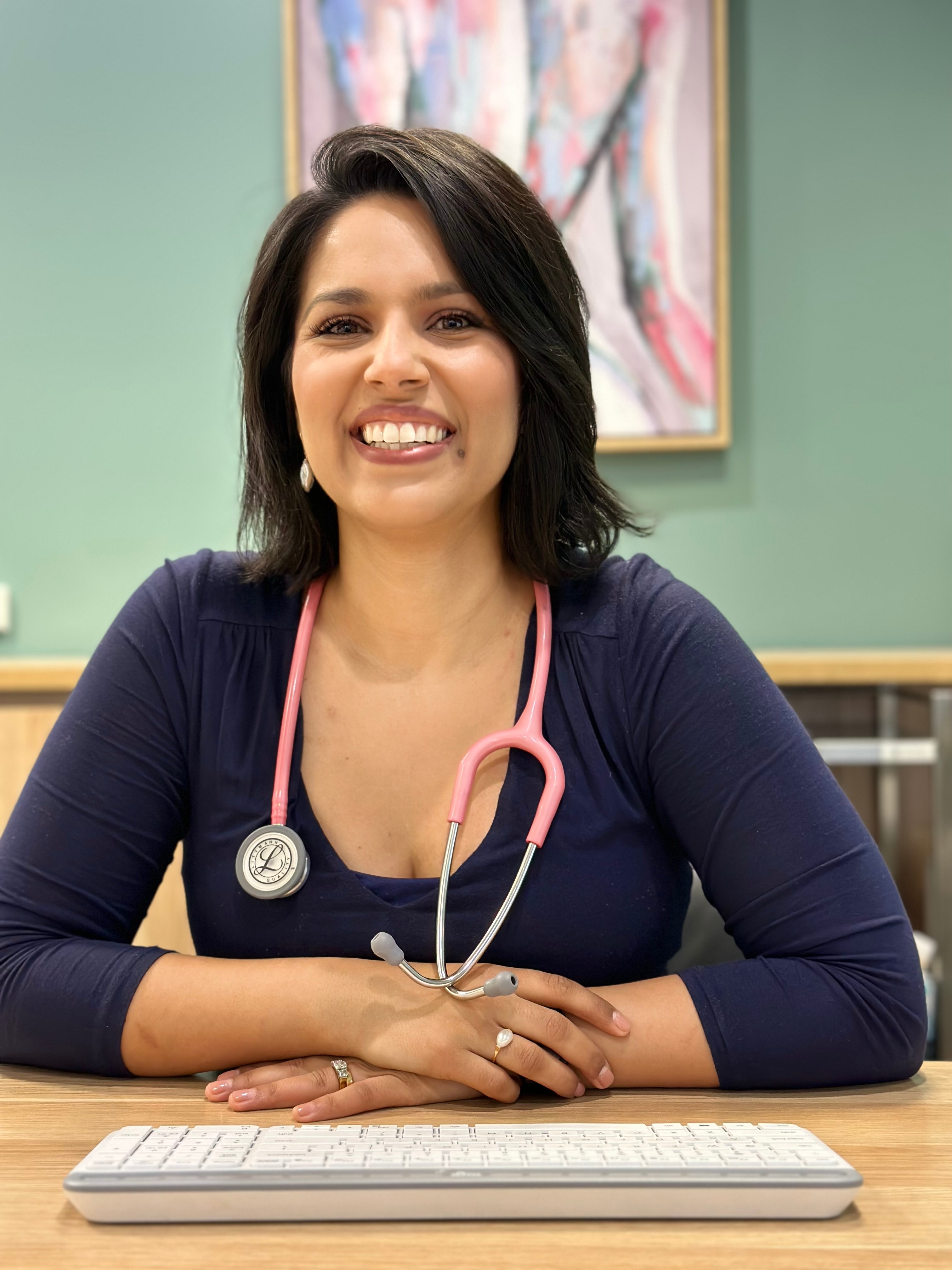 Dr Natasha Vavrek smiles while sitting at a desk. She's wearing a stethoscope around her neck.