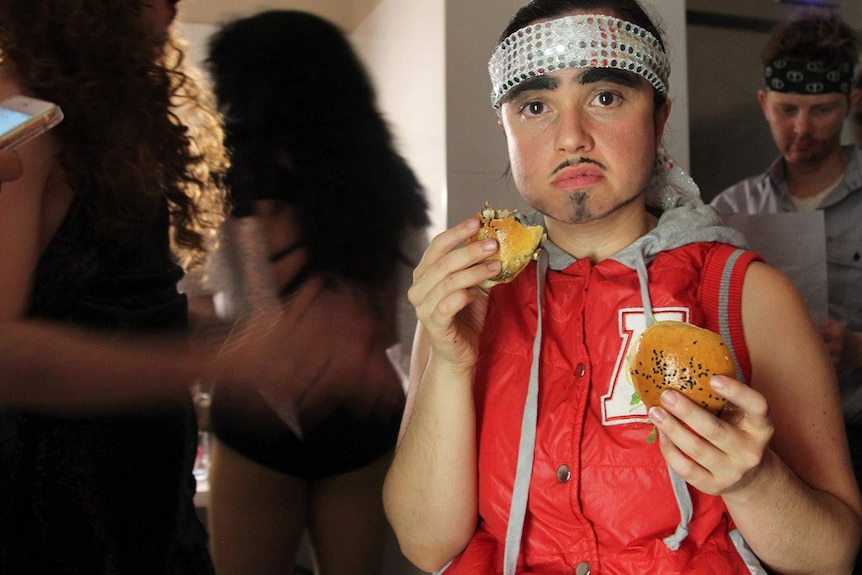 a drag king with sparkly headband holding burgers