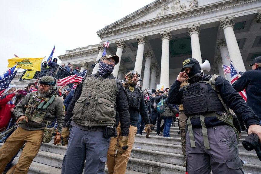People wearing khaki clothes and windbreakers stand on the steps of the Capitol building. 