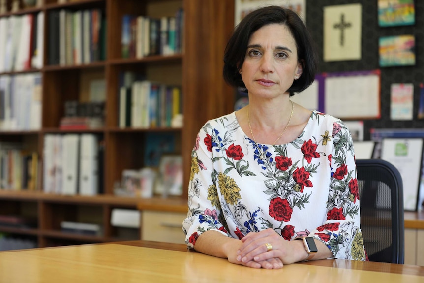 A school principal sits at her desk looking serious.