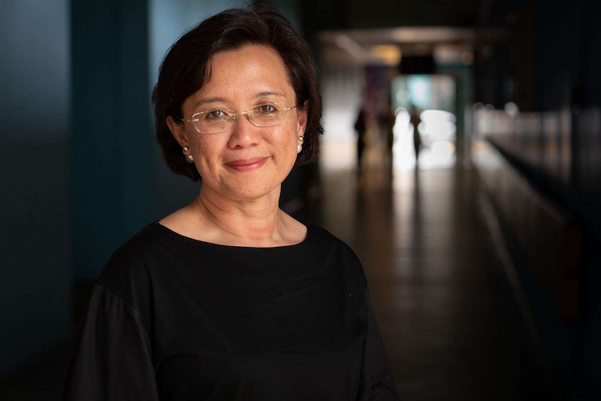 A woman with glasses stands in a university hallway.