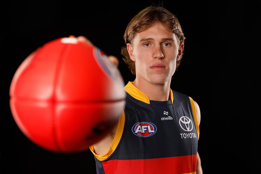 Dan Curtin poses for a photo in his Adelaide jersey holding a football