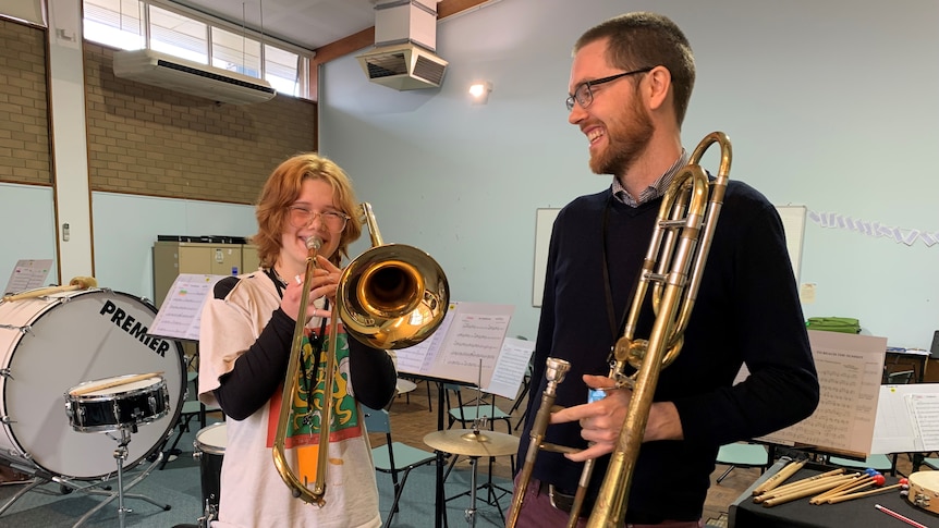 Students Fenella Collins plays a trombone in a music room, watched on by tutor Tim Walsh