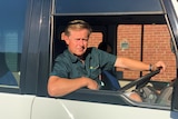 A middle aged man in a mini bus with one hand on the wheel and the other arm resting on the open window
