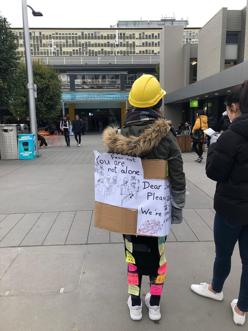 A protestor wears a hardhat and a sign saying "fear not, you are not alone".