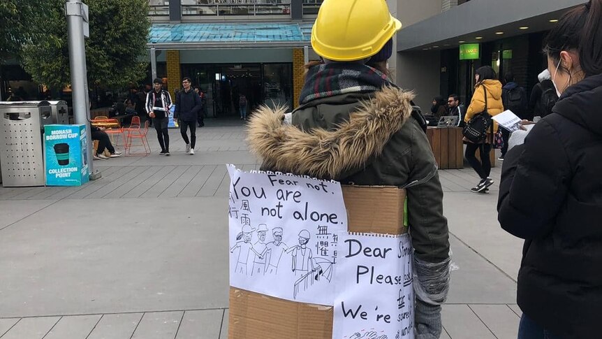A protestor wears a hardhat and a sign saying "fear not, you are not alone".