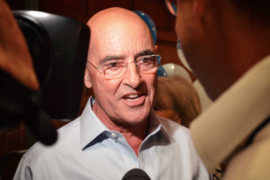 South Australian Liberal President John Olsen speaks to a journalist. He's wearing a blue shirt and glasses.