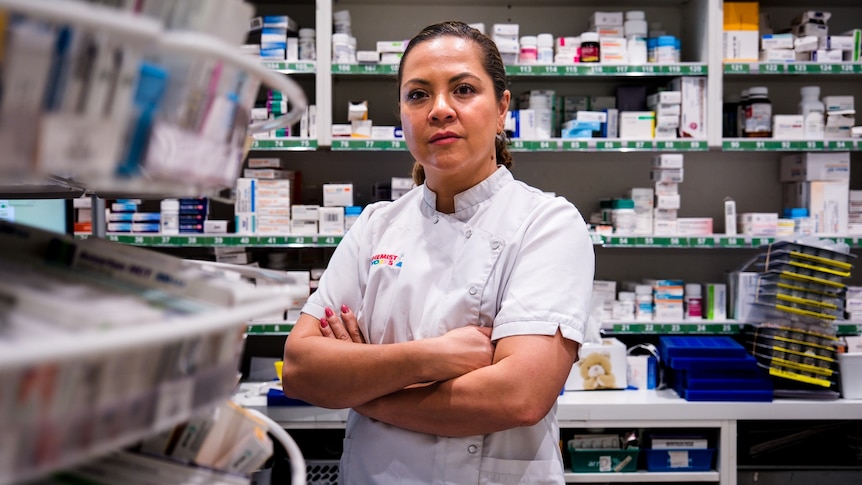 a woman pharmacist standing with her arms crossed inside a chemist
