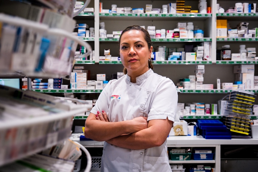 a woman pharmacist standing with her arms crossed inside a chemist