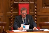 A man sitting in a large red velour and wooden chair