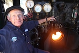 An older man sits in the cab of his steam engine train