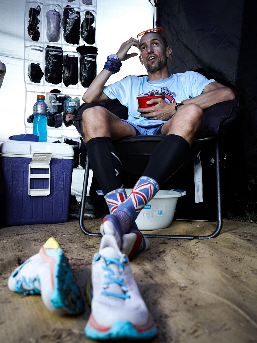 Man sits on chair in running gear, shoes off in foreground.