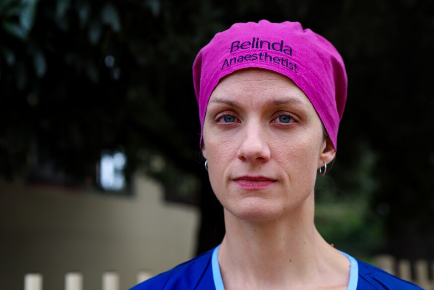 Belinda Phillips wearing pink bandana and blue scrubs standing in front of tree