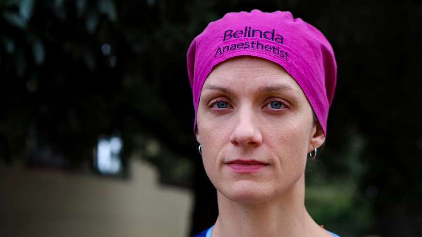 Belinda Phillips wearing pink bandana and blue scrubs standing in front of tree