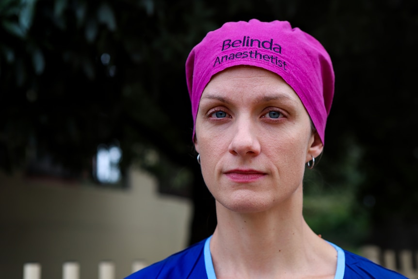 Belinda Phillips wearing pink bandana and blue scrubs standing in front of tree