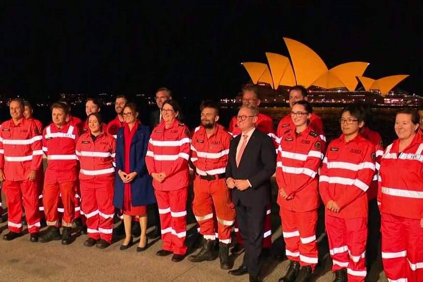 Group of people wearing orange uniforms stand in front of Sydney Opera House.