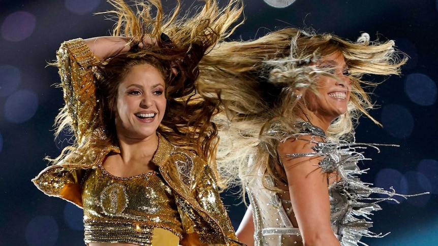 Two women with flowing hair smiling and performing on stage
