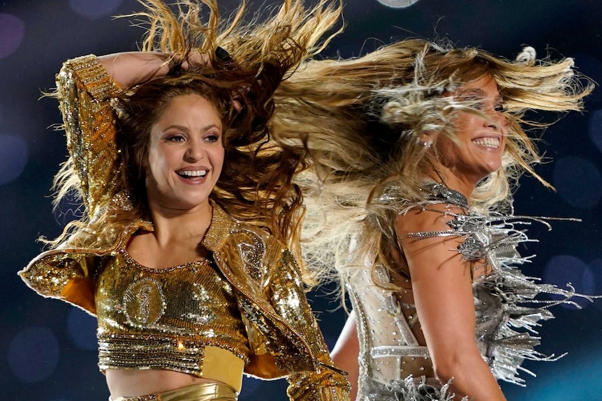 Two women with flowing hair smiling and performing on stage