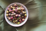 An aerial view of round, multi-coloured (pink, green and yellow) berries in a bowl.