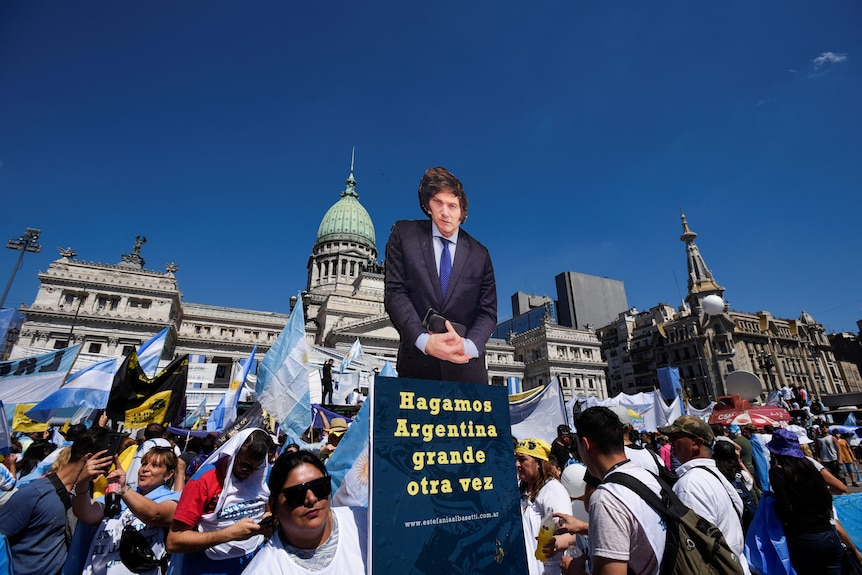 a person holds up a cardboard cutout of president-elect milei , surrounded by other supporters holding argentine flags
