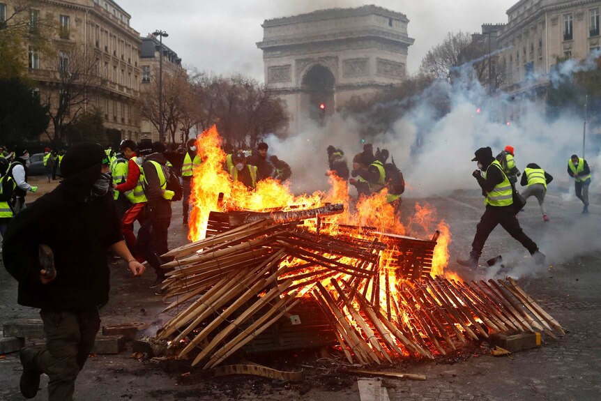 Dozens of protesters wearing yellow vests run from a fire they lit from pieces of wood in a Paris street, creating smoke