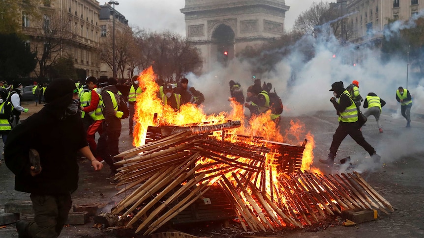 Dozens of protesters wearing yellow vests run from a fire they lit from pieces of wood in a Paris street, creating smoke