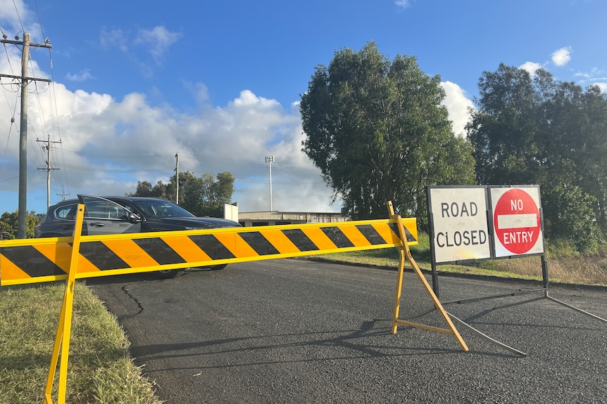 A Road Closed sign and hazard sign in the foreground with a shed and some smoke in the background. 