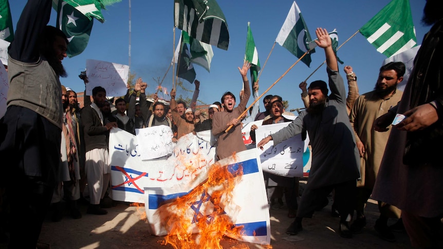 A group of protestors are seen chanting and burning Israeli and US flags.