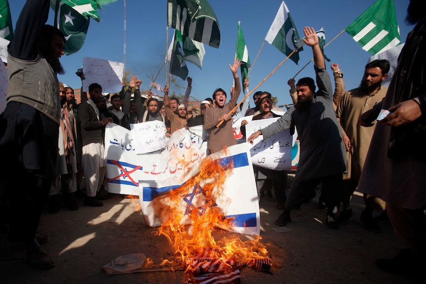 A group of protestors are seen chanting and burning Israeli and US flags.