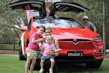 woman and two young children crouched in front of red car with sides open
