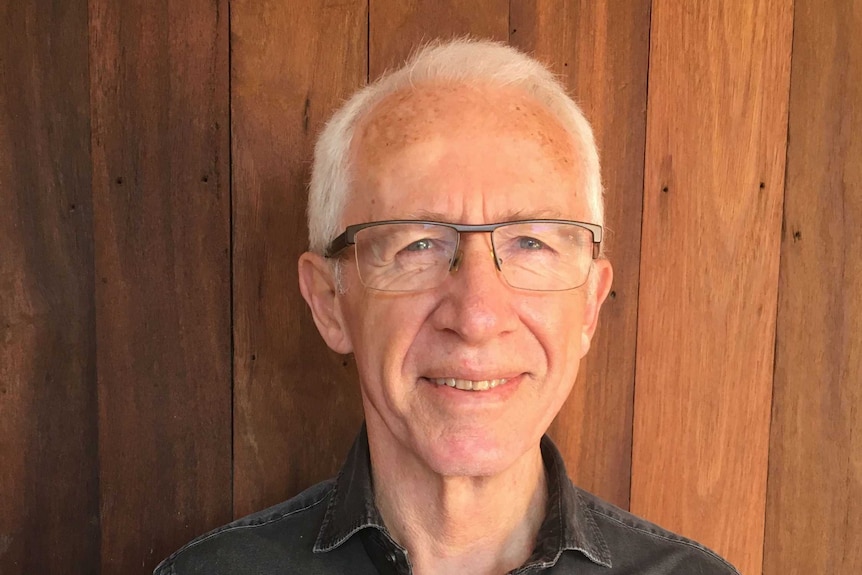 Anthropologist Michael Gallagher stands in front of a wall with wooden panels