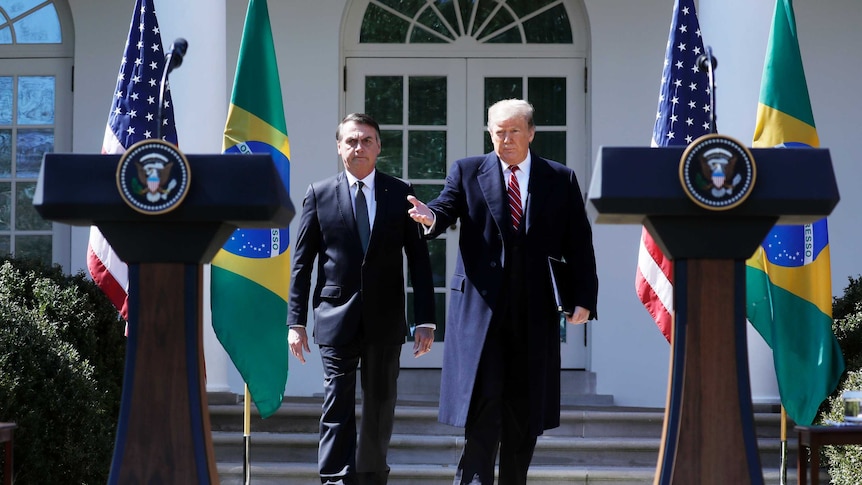 Jair Bolsonaro and Donald Trump walk past flags of their nations towards lecterns set up in the Rose Garden.