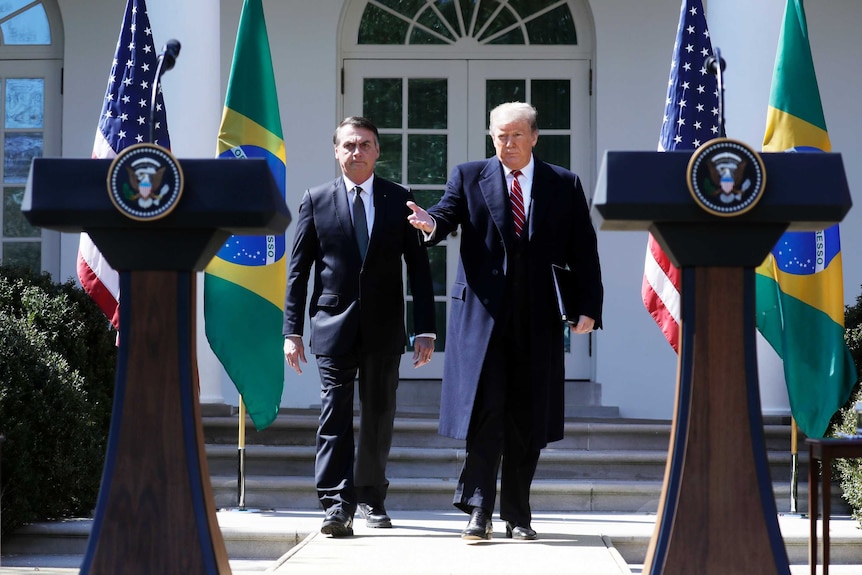 Jair Bolsonaro and Donald Trump walk past flags of their nations towards lecterns set up in the Rose Garden.