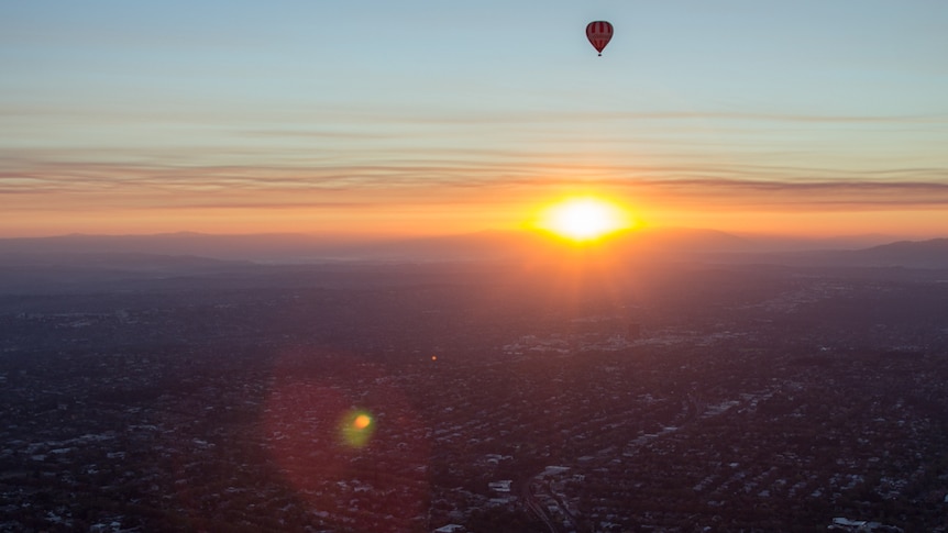 Sunset over mountains, city suburbs in foreground, hot air balloon in the sky