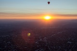Sunset over mountains, city suburbs in foreground, hot air balloon in the sky