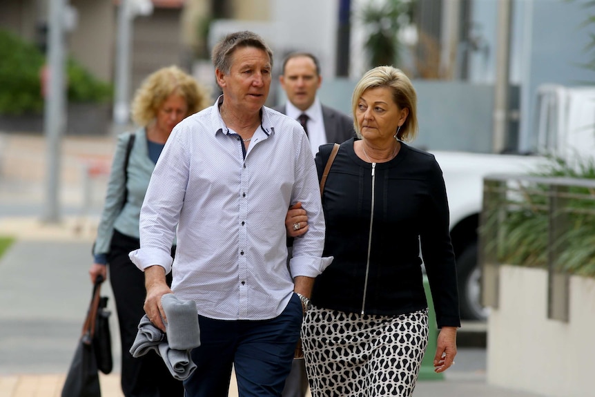 A man, supported by a woman, walks outside a court building.