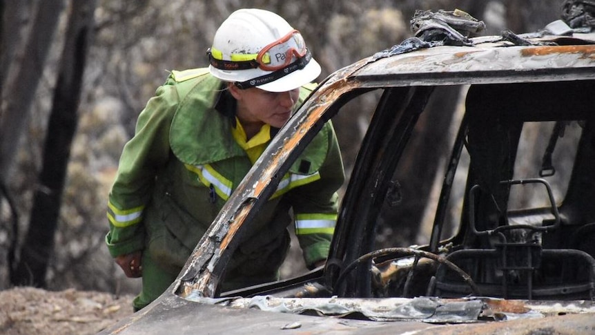 A firefighter inspects a burnt car.