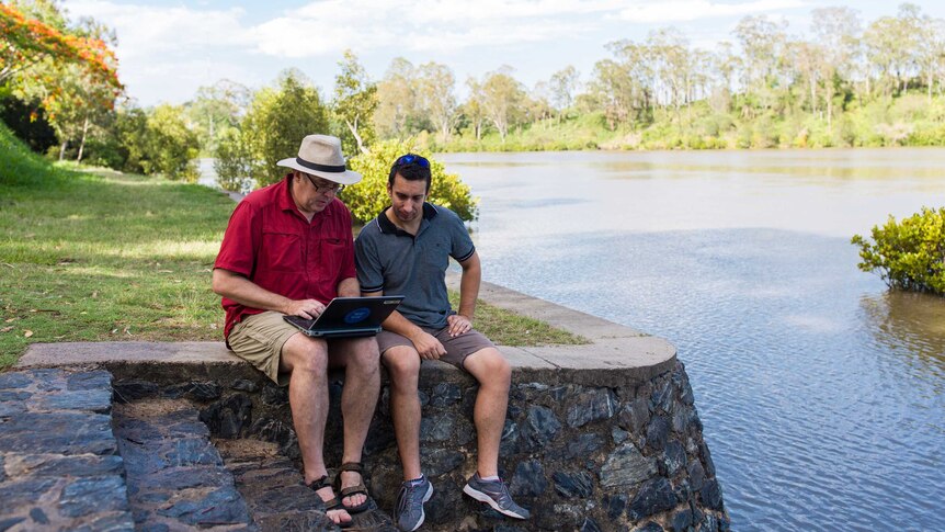 Dr Simon Linke (l) sits with a colleague on the edge of a waterway studying the sounds of fish made in nature.